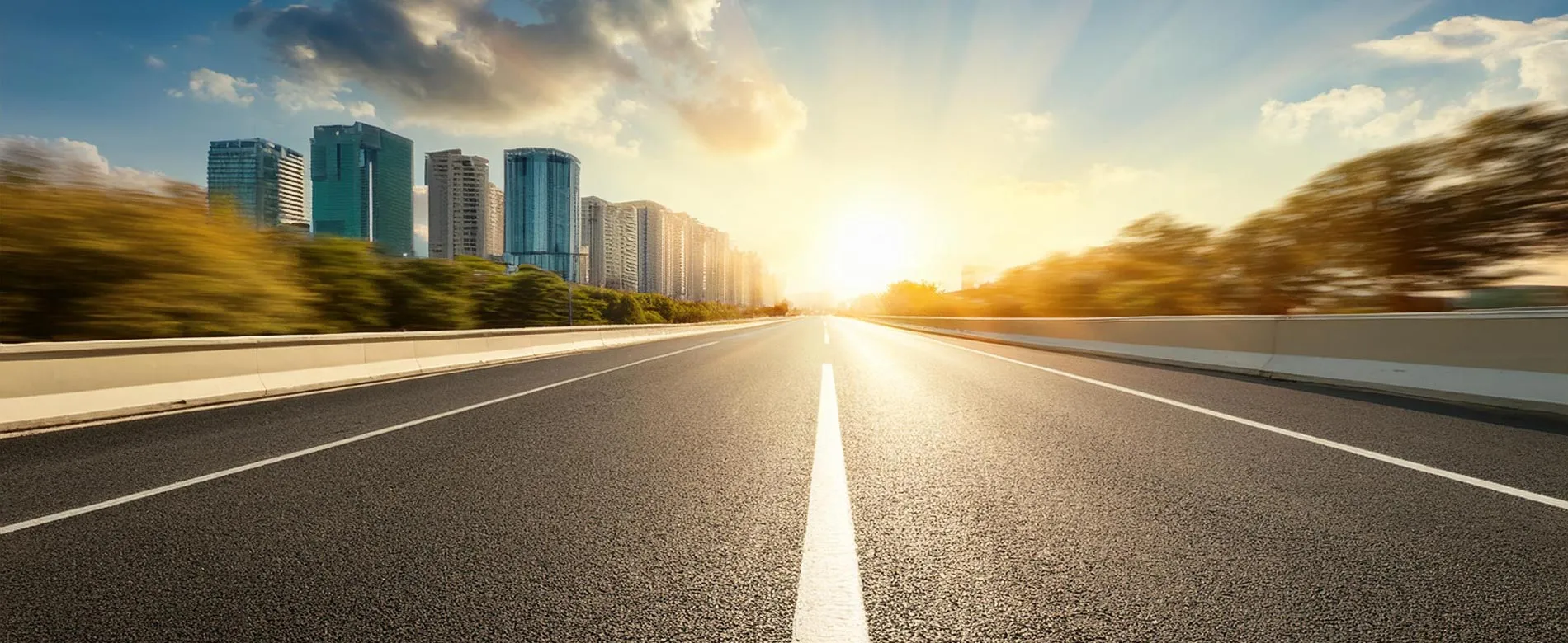 Straight road with sunrise in front heading towards a city with skyscrapers